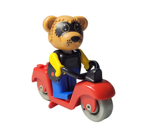 Tan raccoon toy figure with black mask markings sitting on red scooter with blue seat and handlebars.
