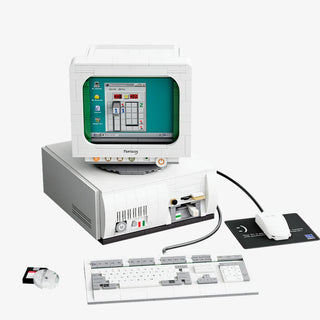 White desktop computer with teal monitor, keyboard, mouse, and floppy disk, styled as 1990s-era PC setup.