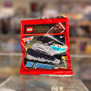 Red foil pack containing LEGO Star Wars TIE Striker minifigure set with black and white spacecraft visible through window.