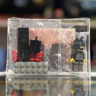 LEGO Castle set 6028 containing black and red brick pieces, gray baseplate, and minifigure with yellow hands in clear plastic