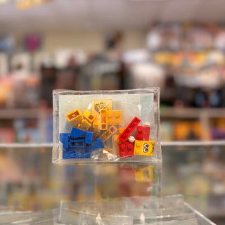 Clear polybag containing colorful plastic building bricks in yellow, blue, and red with a small yellow character head piece.