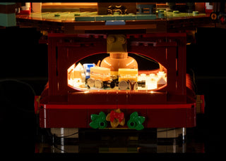 Red LEGO Christmas tree structure with warm white LED lights illuminating interior compartments and green wreaths with red bo