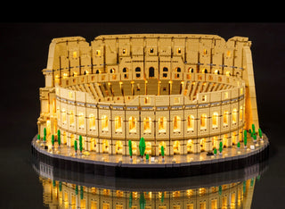 Tan LEGO Colosseum model with warm white LED lights illuminating the structure and green decorative elements on the base.