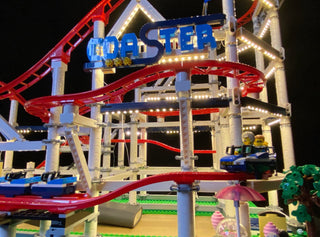 Illuminated LEGO roller coaster set with red track, blue supports, lit signage, and miniature figures on a green base platfor