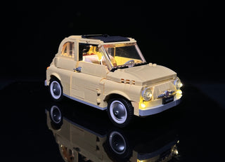 Cream-colored LEGO Fiat 500 model with illuminated headlights, interior, and dashboard against black background.
