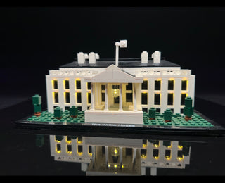 White House LEGO set with yellow LED lights installed in windows, roof fixtures, and interior spaces on black display base.