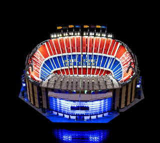 LEGO Camp Nou stadium model illuminated with white overhead lights, red and blue seating sections, and blue base lighting.