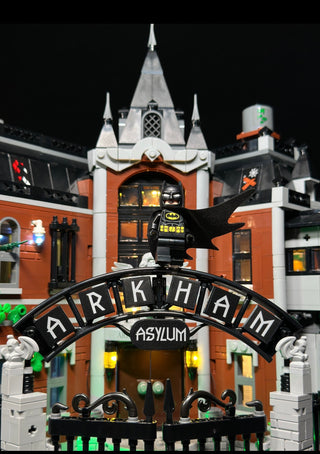 LEGO Arkham Asylum building with illuminated windows, towers, entrance arch, and Batman minifigure displayed with custom ligh