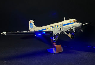 LEGO Douglas DC-3 Pan Am airliner with blue LED lighting on stand against dark background.