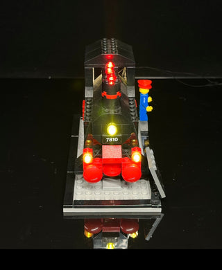 LEGO train set 7810 with illuminated red and yellow lights on engine, cars, and signal tower against dark background.
