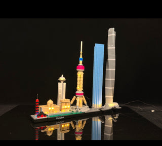 LEGO Shanghai skyline set with illuminated buildings including red pagoda, yellow tower, blue skyscraper, and gray tower on b