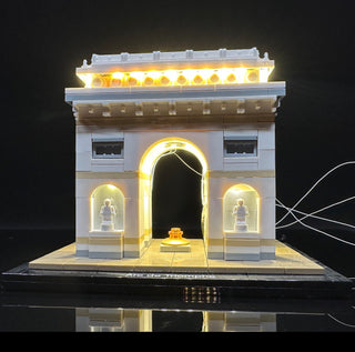 LEGO Arc de Triomphe model with yellow LED lighting illuminating the top cornice, arched entrance, side alcoves, and interior