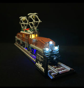 LEGO Crocodile Locomotive with illuminated pantograph, cabin windows, front headlights, and base platform against dark backgr