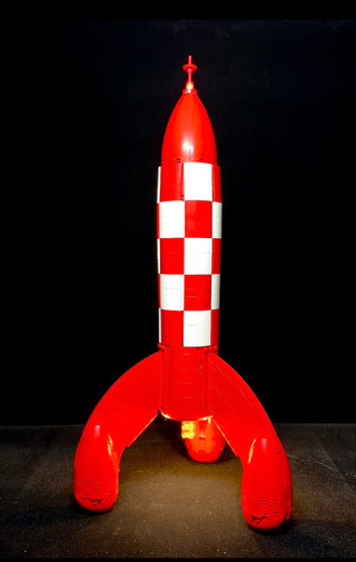 Red and white checkered rocket with pointed nose cone and four fins, illuminated with red and white LED lights against black 