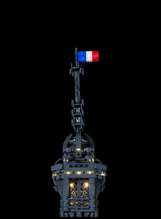 LEGO Eiffel Tower model with illuminated sections and French flag on top against black background.