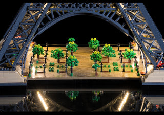 LEGO Eiffel Tower set with illuminated green trees and warm LED lights under the monument's arch at night.