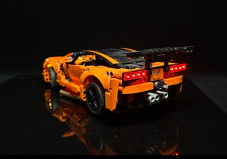 Orange and black LEGO Corvette ZR1 with illuminated red tail lights and front headlights against dark background.