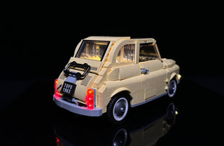 LEGO Fiat 500 car model with illuminated interior, headlights, and red tail lights against black background.