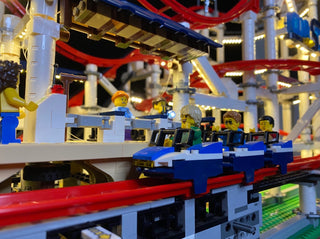 LEGO roller coaster set with illuminated red and yellow track, blue support structure, and minifigures in cars.