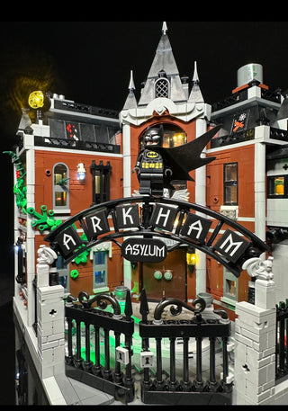 Illuminated LEGO Arkham Asylum building set with yellow and green lights, featuring castle architecture, minifigure, and "Ark