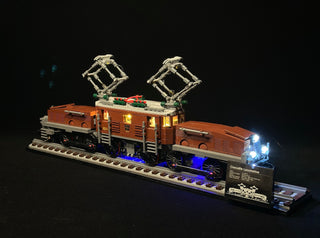 LEGO Crocodile Locomotive set with illuminated windows, pantograph poles, and blue LED undercarriage lighting on display base