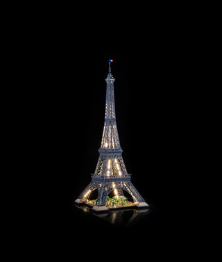 LEGO Eiffel Tower model illuminated with warm white and green LED lights throughout the structure against a black background.
