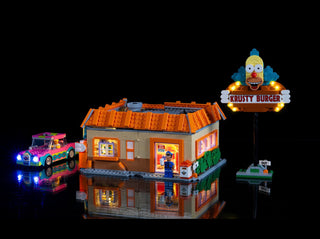 Illuminated LEGO Krusty Burger restaurant building with glowing car and neon sign against black background.