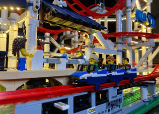 Illuminated LEGO roller coaster set with red track, blue support structure, minifigures, and warm white LED lights throughout