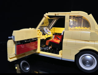 Cream and yellow LEGO Fiat 500 model with open door and hood, illuminated interior and headlights against black background.