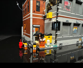 Illuminated LEGO Arkham Asylum set with orange and gray building sections, yellow lighting elements, minifigures, and street 