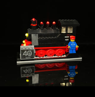 LEGO train set with illuminated red and yellow lights on black locomotive, red wheels, "40 YEARS" emblem, and blue minifigure
