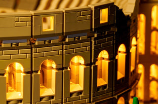 Illuminated LEGO Colosseum architecture set with warm yellow LED lights in arched windows and openings.