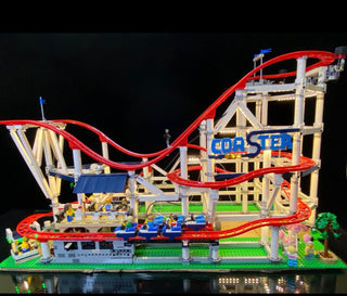 LEGO roller coaster set with illuminated red track, wooden support structure, blue cars, and lit base platform against dark b