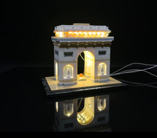 LEGO Arc de Triomphe building set with warm white LED lights illuminating the arches, windows, and roofline against black bac
