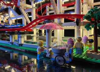 Illuminated LEGO roller coaster set with lit red track, colorful minifigures, and carnival stand with glowing lights througho