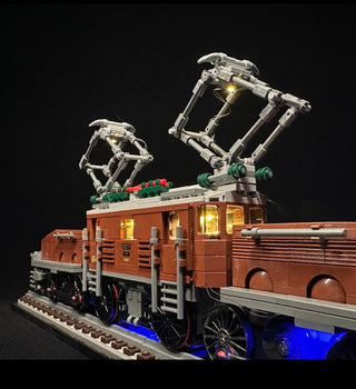 Brown and cream LEGO locomotive with illuminated windows, pantograph arms, and blue undercar lighting on track base.