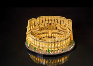 Illuminated LEGO Colosseum model with warm yellow lights throughout the structure and base against dark background.