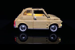 Cream-colored LEGO Fiat 500 with illuminated headlights, interior lights, and red taillights against black background.