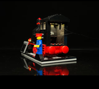 Illuminated LEGO train set with red and blue locomotive, glowing red lights on engine and wheels, black cabin with lit window
