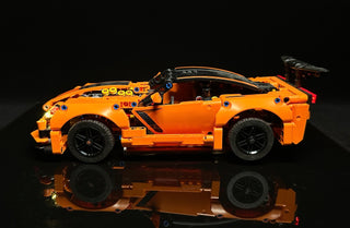 Orange LEGO Chevrolet Corvette ZR1 with illuminated headlights, interior lights, and dashboard details against black backgrou
