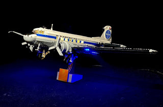 LEGO Douglas DC-3 Pan Am airliner with blue LED lighting illuminated on display stand against dark background.