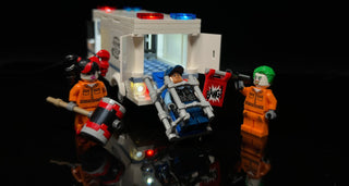 LEGO Arkham Asylum set with illuminated red and blue roof lights, lit interior cell, and glowing minifigure accessories on bl