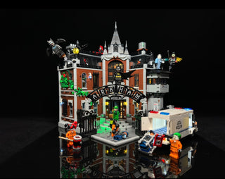 Illuminated LEGO Arkham Asylum set 76300 with lit windows, interior details, and surrounding minifigures and accessories disp
