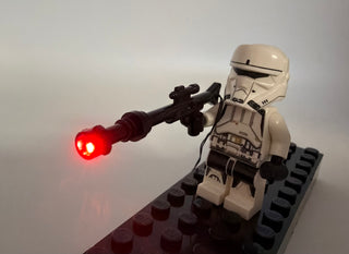 White minifigure holding black blaster rifle with red flashing LED light at muzzle, mounted on baseplate.