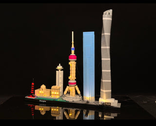 Illuminated LEGO Shanghai skyline set featuring lit buildings and towers on black base against dark background.