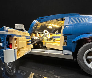 Blue and tan LEGO Ford Mustang GT with illuminated interior, hood open to reveal lit engine and detailed chassis.