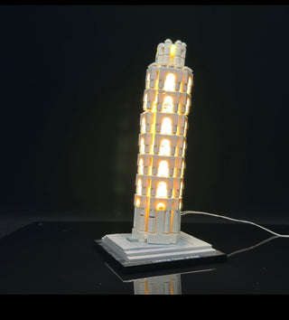 Illuminated LEGO Leaning Tower of Pisa model with warm white lights in multiple levels and base, power cord visible.