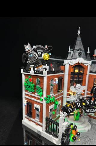 Illuminated LEGO Arkham Asylum set with Batman minifigure, green vines, lit windows, yellow clock, and colored interior light