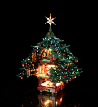 Illuminated LEGO Christmas tree with lit star topper, green branches, red and white ornaments, miniature house interior, and 
