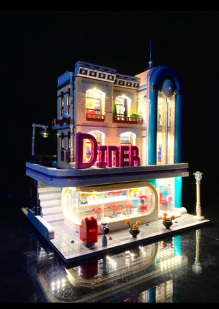 Illuminated LEGO Downtown Diner set with warm interior lights, red neon "DINER" sign, blue exterior accents, and street lamp 